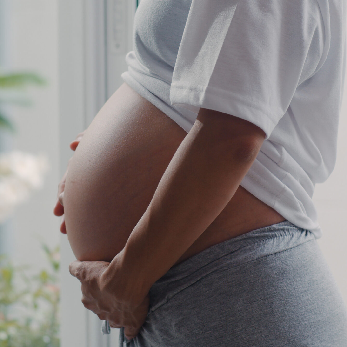 Young Asian Pregnant woman holding her belly talking with her child. Mom feeling happy smiling positive and peaceful while take care baby, pregnancy near window in living room at home concept.
